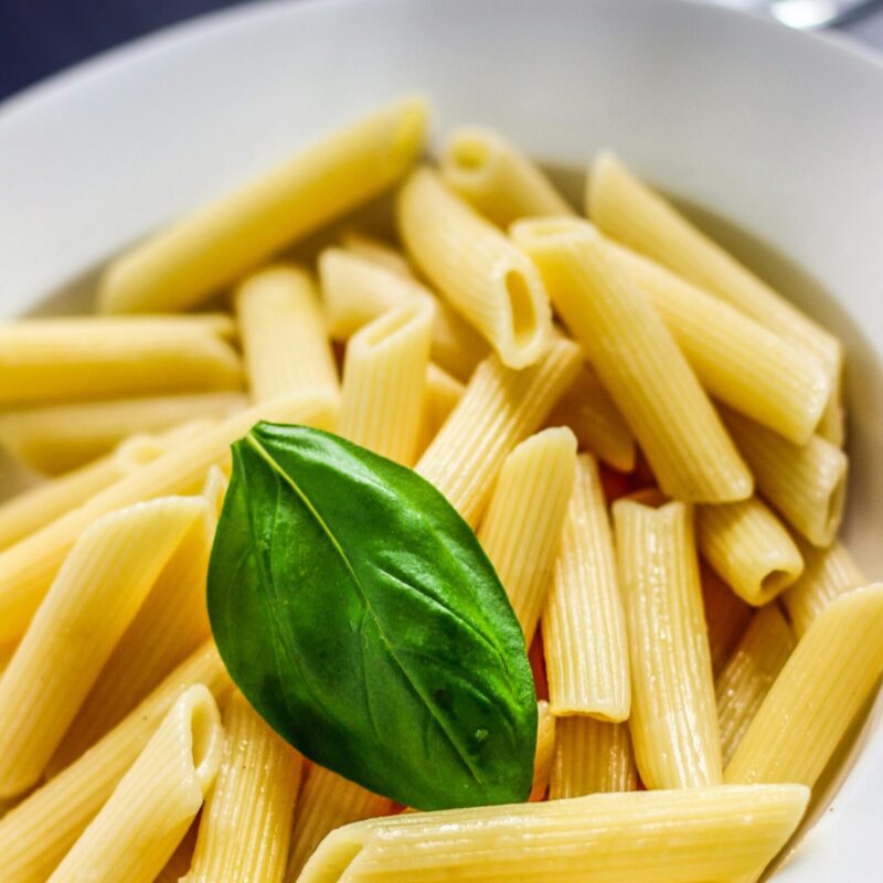 Close-up of savory penne pasta with a fresh basil garnish in a white bowl.