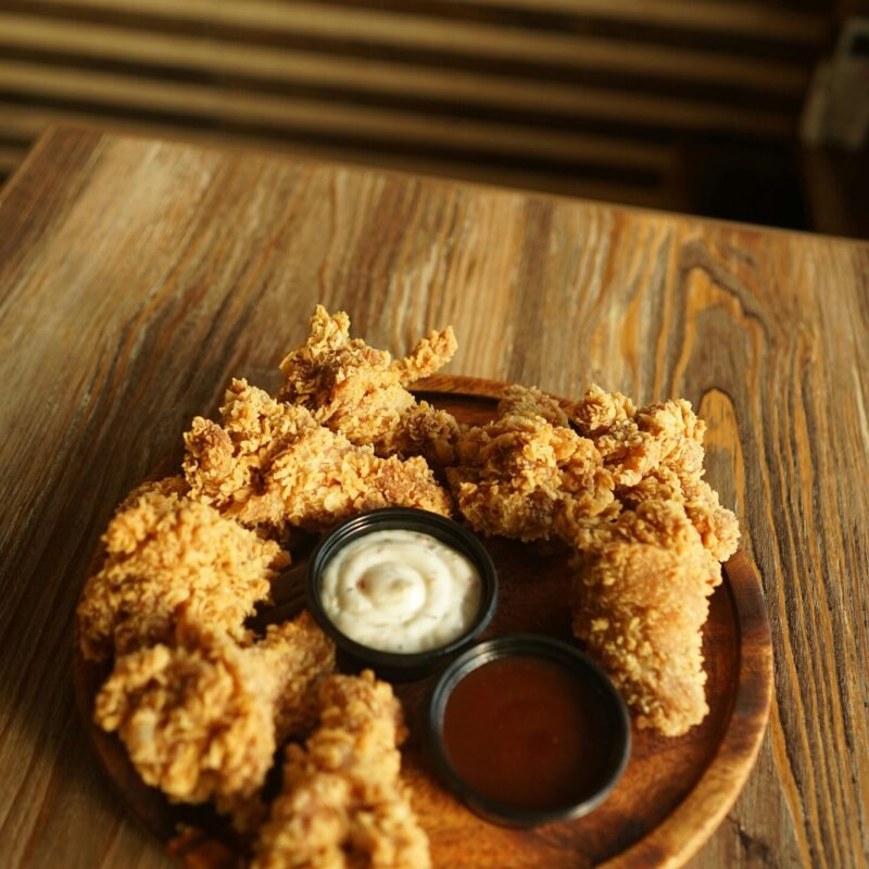 Delicious crispy fried chicken served with two tasty dipping sauces on a wooden plate.